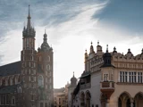 Historiske bygninger på Krakóws hovedmarkedsplads ved solnedgang, med Mariakirken til venstre og Klædehallen til højre, under en delvist overskyet himmel.