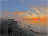 En fredfyldt solnedgang over roligt vand med orange og lyserøde skyer på himlen og en klippekyst til venstre, der reflekterer det farverige lys.