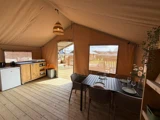 Et hyggeligt glampingtelt med et lille køkken, et spisebord med plads til fire og store vinduer med udsigt til et trædæk og den udendørs natur.