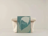 En beige stofpose står bag en grøn bog med et hvidt abstrakt blomstermotiv og teksten "TEAM DR JOSEPH" på omslaget.