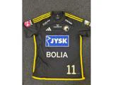 En sort og gul sportstrøje med sponsorlogoer, nummer 11 og et cirkulært emblem på brystet, der lå fladt på et mørkt tæppe.
