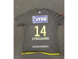 En sort sportstrøje med gule kanter, hvor der på ryggen står navnet LYNGGAARD, nummer 14 og sponsorerne JYSK og SOFACOMPANY, lå fladt på et tæppebelagt gulv.