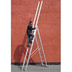 En person klatrer op ad en høj, udstrakt aluminiumsstige med en støtteramme, der er placeret mod en rød murstensvæg udendørs.