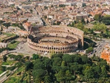 Luftfoto af Colosseum i Rom, Italien, omgivet af historiske bygninger, veje og grønne træer.