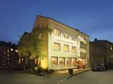 Et veloplyst, treetagers hotel ved navn Hotel Tom Kyle står på et gadehjørne i skumringen med et træ og parkerede biler i nærheden.