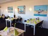 En moderne restaurant med hvide borde, sorte stole og gulgrønne servietter. Tulipaner pryder bordene, og store malerier af kystscener hænger på den hvide væg.