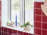En vindueskarm med et blåt stearinlys, en potteplante, en beige beholder med en badesvamp og en børste mod en væg af røde fliser.