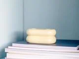 En cremefarvet, afrundet keramikgenstand sidder oven på en stak bøger eller magasiner mod en lyseblå væg.