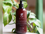 En flaske Grums The Kind Hand Lotion står foran grønne blade. Den brune flaske har en sort pumpe og en hvid tekst, der beskriver dens fugtgivende og reparerende egenskaber.