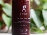 En rødbrun flaske med etiketten grums The Kind Hand Lotion med tekst om hydrering, reparation af barriere og ingredienser på en bladgrøn baggrund.