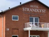 En murstensbygning med en hvid balkon og ordene HOTEL STRANDLYST på facaden. Nummeret 18 er synligt på væggen.