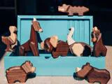 Et sæt udskårne dyrefigurer i træ, bl.a. en giraf, en elefant og en bjørn, udstillet på og omkring en blågrøn kasse på en træoverflade.