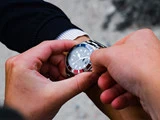 Nærbillede af to hænder, der justerer et sølvfarvet armbåndsur på en persons håndled, med urskiven tydeligt synlig.