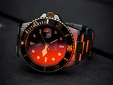 Nærbillede af et sølvfarvet og sort armbåndsur med gulddetaljer, oplyst af et orange lys, der hviler på en mørk overflade.