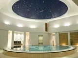 En cirkulær indendørs pool under et kuppelformet loft med en stjerneklar nattehimmel skaber en afslappende og luksuriøs atmosfære.
