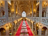 En storslået bibliotekssal med højt hvælvet loft, buede vinduer, udsmykkede søjler, bogreoler og en gang med rødt tæppe og borde med bøger.