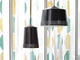 To moderne, sorte pendellamper hænger foran et vindue med et geometrisk gult og grønt mønstret gardin.