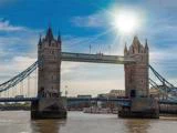 Tower Bridge i London over Themsen på en solrig dag, hvor solen skinner, og bådene er synlige på vandet.