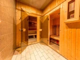 To saunaer i træ med glasdøre ligger side om side i et spa-anlæg med klinkegulv og varm belysning.