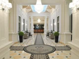 Elegant hotellobby med lysekroner, hvide søjler, klinkegulv, potteplanter, sofaer og et rundt tæppe med påskriften Hotel President ved indgangen.