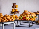Et bord med forskelligt bagværk, muffins og et fad med frisk frugt i skiver, herunder vindruer, æbler og bær.