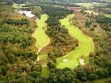 Luftfoto af en golfbane omgivet af træer med fairways, sandbunkers og en lille dam blandt frodige grønne områder.