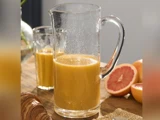 En glaskande og et glas fyldt med appelsinjuice står på et træbord ved siden af skiveskåret grapefrugt og en croissant.