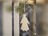 En enkel, flad, hvid engel med glorie hænger på en fyrretræsgren ved et vindue, dekoreret med stjerneformede lyskæder.