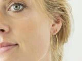 Nærbillede af en kvindes ansigt med fokus på hendes øre, der er prydet med en lille guldørering og en stor struktureret guldørering.