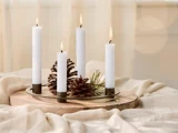 Fire tændte hvide lys i forskellige højder er arrangeret på en rund træbakke med kogler og en fyrretræsgren på et blødt beige klæde.