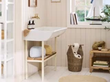 Et lyst, hyggeligt badeværelse med en hvid håndvask, flettede kurve, en toiletrulle, toiletartikler og en model af en sejlbåd på vindueskarmen.