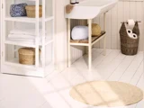 Et lyst, pænt badeværelse med en hvid vask, flettede kurve, håndklæder på hylder, et rundt tæppe og en flettet skraldespand med toiletruller.