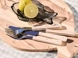 En fiskeformet glasskål med limefrugter står på et skærebræt af træ ved siden af to gafler og to knive med lyse træhåndtag.