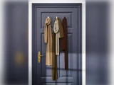 Tre strikkede tørklæder i brune og beige nuancer hænger på kroge på en lukket mørkeblå dør med guldhåndtag, oplyst af blødt naturligt lys.