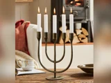 En metalmenorah med fem tændte hvide lys står på et træbord med en kop, en skål og brænde i den hyggelige baggrund.