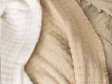 Nærbillede af tre krøllede, strukturerede stoffer i hvid, beige og brun med synlige syninger og flossede kanter.