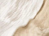 Nærbillede af struktureret stof med et bølget mønster i to farver: råhvid til venstre og beige til højre.