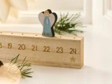 En adventskalenderblok af træ, nummereret fra 19 til 24, med en lille engelfigur placeret over tallet 21.