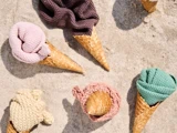 Isvafler på sand, hver fyldt med farverigt sammenrullet strikket stof i stedet for is, i nuancer af pink, brun, creme, grøn og fersken.