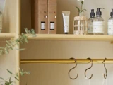 Træhylde med toiletsager, lotionflasker, en lille vase med en blomst og en tom garderobestang nedenunder med to kroge.