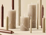 Forskellige søjle- og koniske stearinlys i beige, taupe og burgunder er anbragt både stående og liggende på en neutral baggrund.