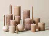En samling af beige og brune stearinlys i forskellige former og størrelser er anbragt på en neutral overflade med en lys baggrund.
