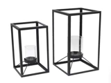 To rektangulære lanterner i sort metal i forskellige størrelser med hver sin lysestage i klart glas inde i den åbne ramme.
