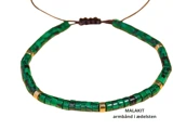 Et perlearmbånd med grønne og guldfarvede cylindriske perler, mærket MALAKIT armbånd i ædelsten på en hvid baggrund.