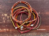 En bunke med 10 farverige perlearmbånd i nuancer af rød, orange, pink og guld på en træoverflade. Teksten lyder 10 armbånd.