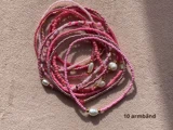 Ti lyserøde perlearmbånd, nogle med perler og gulddetaljer, er arrangeret i en bunke på en beige overflade. Teksten 10 armband står i nederste højre hjørne.