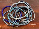Ti perlearmbånd i blå, sorte, gyldne og hvide toner er arrangeret på en brun træoverflade. Teksten 10 armband står i nederste højre hjørne.