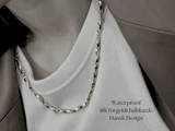 En person iført en hvid ribbet top, en beige blazer og en guldkæde. Teksten lyder: Vandtæt 18k forgyldt halskæde Dansk Design.