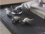 Tre sølvindpakkede bolsjer ligger på en sort bakke ved siden af en dekorativ glasbeholder og en bog med delvis synlig omslagstekst.