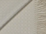 Nærbillede af et cremefarvet vævet stof med et geometrisk mønster, foldet diagonalt og med frynser på den ene kant.